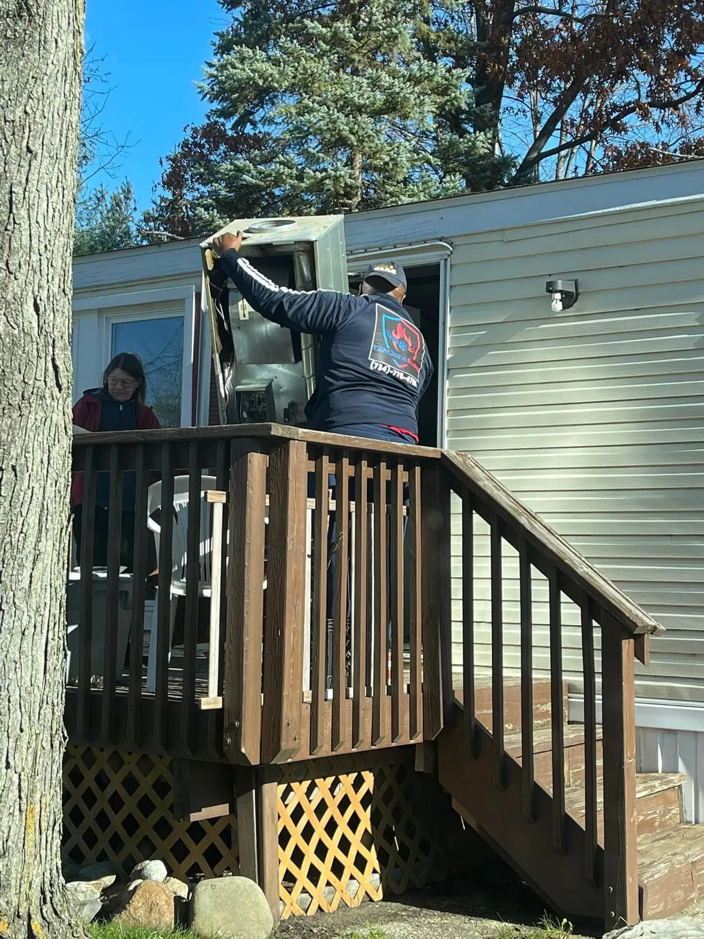 Al from Temprasure lifting a panel off a package unit while the homeowner watches from the deck