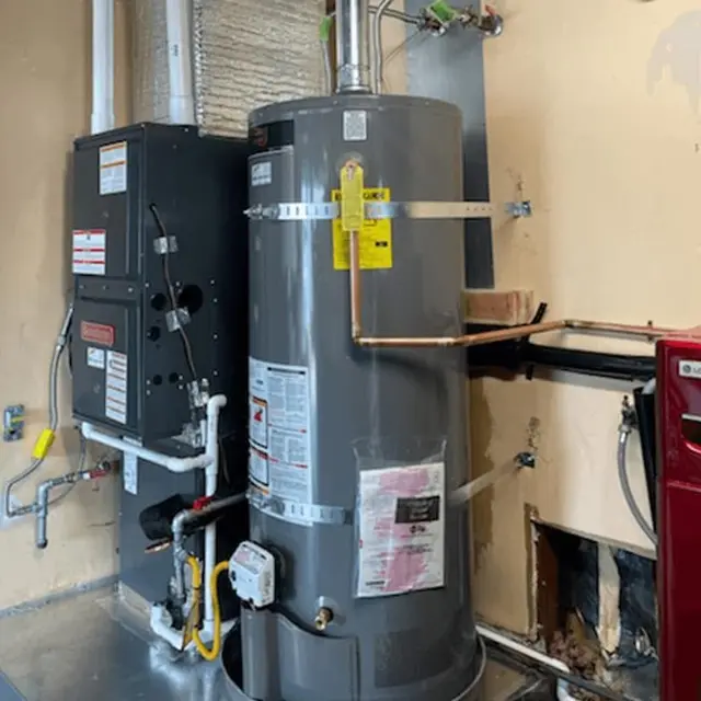 A Goodman furnace and a strapped Rheem water heater installed side by side in a utility room